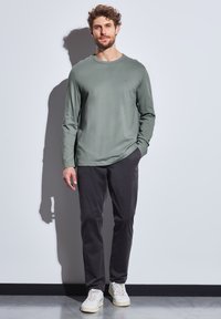 Pitkähiha, oliivinvihreä T-paita pyöreällä pääntiellä, yhdistetty tummiin housuihin ja valkoisiin tennareihin. Yksinkertainen muotoilu, sileä pinta.