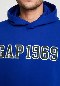 Sudadera de algodón azul con una gran impresión "GAP 1969" en blanco y verde, con un cuello interior acanalado texturizado.