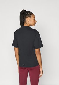 Čierne športové tričko s krátkym rukávom, okrúhlym výstrihom, hladkou textúrou a prešitím; v kombinácii s tmavými červenými legínami.