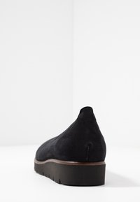 Zapato de ante negro con una suela baja y gruesa y un talón ligeramente puntiagudo. El diseño presenta una textura suave sin patrones visibles.