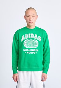 Žalias megztinis su balta spausdinta užrašu "ADIDAS WORLDWIDE HOOPS", su apvalia iškirpte ir banguotomis rankovėmis.