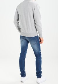 Sudadera gris de cuello redondo, diseño ajustado, con puños y dobladillo acanalados. Combinada con jeans ajustados azules y zapatillas blancas, vista desde la parte posterior.