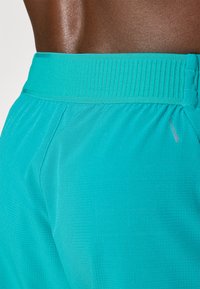 Turquoise sportshorts van een gestructureerde stof, met een elastische tailleband en subtiele merkdetails, die comfort en flexibiliteit benadrukken.