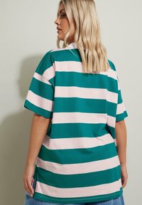 Randig T-shirt i teal och ljus rosa, med korta ärmar, en lös passform och sidslitsar för ökad komfort. Klassisk rund halsdesign.