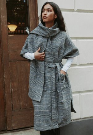 Harmaa-musta ruudullinen kudottu takki, jossa korkea kaulus, vyötärösolki ja ylisuurennetut hihat, taskuilla ja tekstuuripinnalla.