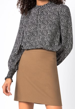 Femme portant un chemisier à manches longues noir et blanc à motifs, rentré dans une jupe trapèze taille haute de couleur beige.