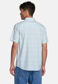 Short-sleeve light blue shirt with a subtle wave pattern, button-down collar, and curved hem, made from a lightweight fabric.
