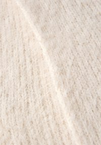Tissu tricoté blanc avec une texture duveteuse et un subtil motif de côtes verticales. Montre des fils de laine fins et légers.