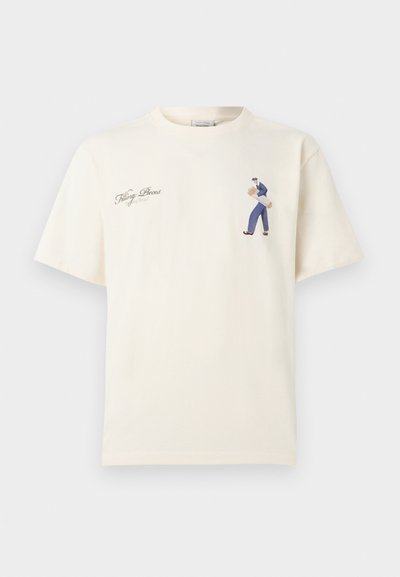 Εκρού T-shirt με μικρό γραφικό ενός ατόμου που κουβαλάει ξύλα στη δεξιά πλευρά του στήθους και κειμενογραμμή με καλλιγραφικό κείμενο στην αριστερή πλευρά του στήθους.