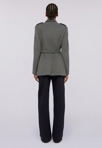 Šedý vlněný kabát s propracovaným střihem, špičatými klopami a páskem v pase, se shoulder epauletami a hladkou texturou.