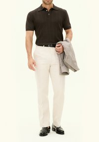 Brun texturerad polo, gräddfärgade skräddarsydda byxor, svart bälte och svarta loafers. Grå rutig blazer hängande över ena armen.