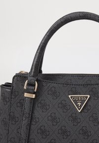 Czarna syntetyczna torebka o teksturowanej powierzchni, zaokrąglonych uchwytach i metalicznym trójkątnym logo. Posiada zamek błyskawiczny oraz złote akcenty metalowe.