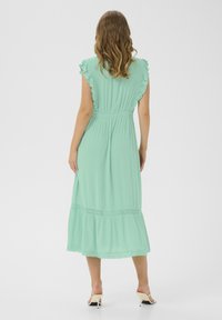 Vestido midi verde menta hecho de tela ligera, con mangas acampanadas, cintura elástica y detalle de encaje en el dobladillo.