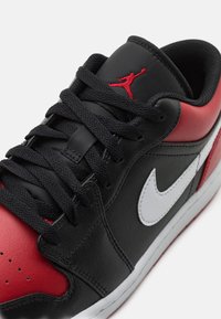 Baskets Nike Air Jordan noires, rouges et blanches avec des lacets noirs, un logo Jumpman rouge sur la languette et un swoosh Nike blanc sur le côté.