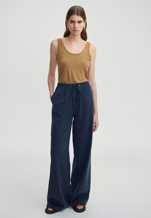 Canotta marrone, pantaloni larghi blu navy con cintura regolabile in vita, sandali piatti. Tessuto morbido con design minimalista e senza motivi visibili.