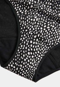 Ropa interior negra con un patrón de puntos irregulares blancos, borde negro y costuras visibles sobre un fondo blanco.