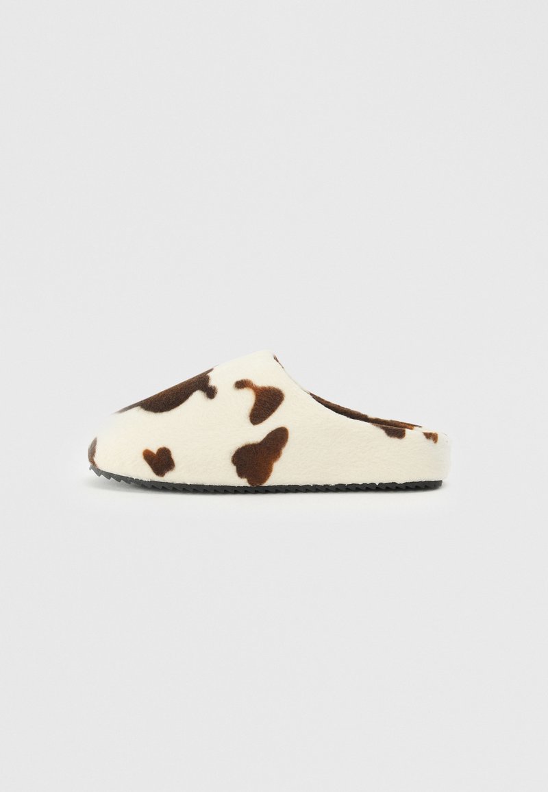 Fleece-lined slip-on slipper with a white base and brown cow print. Round toe and textured black outsole for grip.