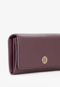 Portafoglio in pelle bordeaux con finitura testurizzata, logo in metallo dorato e design pieghevole. Bordi lisci e linee pulite ne evidenziano la forma.