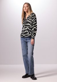 Blouse à manches longues noire et crème avec un motif zèbre, associée à un jean bleu clair et des bottes noires à semelles épaisses. Tissu lisse, coupe décontractée.