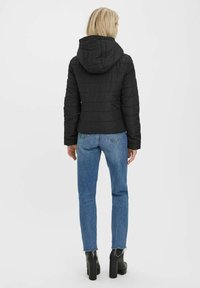 Sort puffermantel med hætte, designet med quiltet mønster og tætsiddende silhuet, parret med blå jeans og sorte platformstøvler.