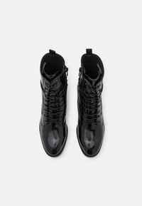 Botines de charol negro con una textura suave, que presentan un diseño de cordones, una cremallera lateral y una puntera redonda.