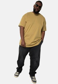 T-shirt a maniche corte oversize di colore beige, abbinato a jeans scuri e strappati. Calzature con un design multicolore e suola chiara.