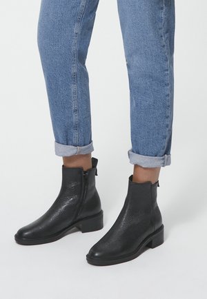 Zwarte leren enkellaarzen met een gestructureerde afwerking, ronde neus, lage blokhak en een rits aan de zijkant. Gecombineerd met opgerolde denim jeans.