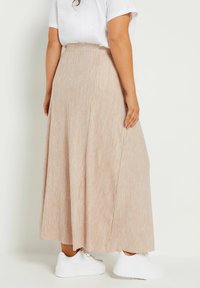 Jasnobeżowa, prążkowana spódnica sięgająca kostek z elastycznym paskiem w talii, zestawiona z białymi sneakersami. Gładka faktura i zwiewna sylwetka.