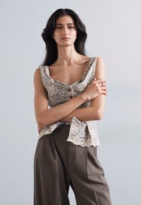 Vaaleanharmaa pitsitoppi, jossa on kukkakuvioita, leveät olkaimet ja napitusyksityiskohta, yhdistettynä väljiin tummanruskeisiin housuihin. Silkkinen pintakuvio.