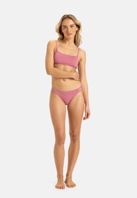 Růžový bikinový set obsahující přiléhavý top s tenkými ramínky a odpovídající nízké spodní díly, obojí vyrobeno z hladké, elastické tkaniny.