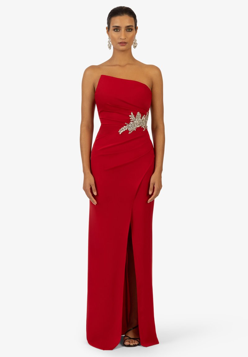 Abito rosso senza spalline con silhouette aderente, spacco laterale e intricate decorazioni in argento in vita. Tessuto morbido e fluido.