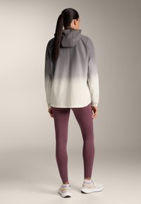 Ľahká bunda v prechode od sivej po bielu, so kapucňou a elastickými manžetami, skombinovaná s bordovými legínami a bielymi športovými topánkami.