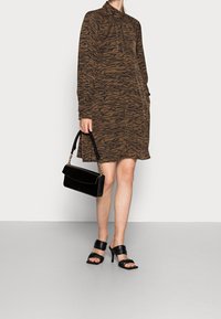 Brun och svart tigerrandig långärmad klänning med hög krage, tillsammans med en svart handväska och svarta högklackade sandaler.