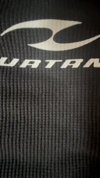 Mustmust tekstuuriga kude, millel on sooneline pind ja silmapaistev valge logo. Materjal näeb välja sportlik ja vastupidav.