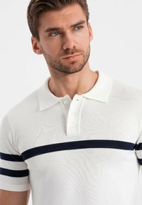 Polo shirt bianco lavorato a maglia con strisce orizzontali blu navy sulle maniche corte, collo con tre bottoni e un tessuto testurizzato.