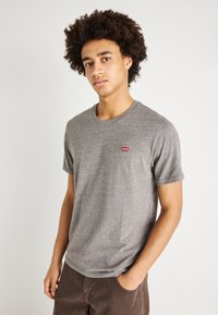 Camiseta de algodón gris con cuello redondo y mangas cortas. Presenta un pequeño logo rojo de Levi's en el lado izquierdo del pecho. Textura suave.