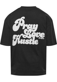 Tricou negru din bumbac cu un text mare alb care spune „Pray Love Hustle” într-un font jucăuș, având un mic logo al mărcii.