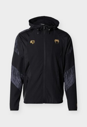 Svart vindjakke med hette, som har gullfargede logoer, gråmønstrede detaljer, glidelåslommer og et strømlinjeformet, atletisk design.