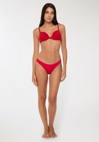 Reggiseno push-up in pizzo rosso con slip coordinati. Il reggiseno presenta una finitura liscia con un fiocco centrale e spalline regolabili.