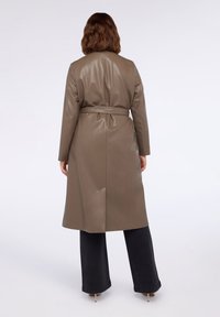 Palton din piele ecologică de culoare verde măsliniu, cu talie încinsă, mâneci lungi și lungime până la jumătatea gambei. Textură netedă și design minimalist.