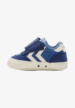 Blauwe stoffen sneaker met een witte rubberen zool, voorzien van een klittenbandsluiting, gladde en gestructureerde delen, en drie witte chevronstrepen aan de zijkant.
