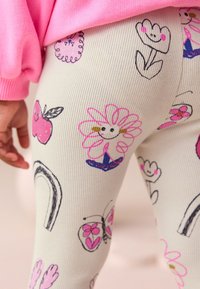 Leggings bianchi a coste con illustrazioni colorate di fiori, frutta, farfalle e un arcobaleno. Tessuto morbido e vestibilità elastica.