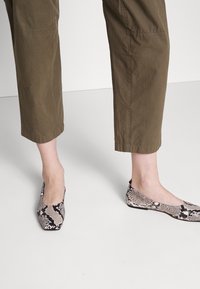 Schlangenleder-Print Ballerinas mit spitzer Zehenform, aus synthetischem Material. Sie zeigen ein Muster in Schwarz, Weiß und Beige. Kombiniert mit olivgrünen, knöchellangen Hosen.