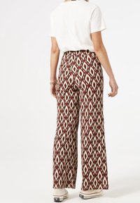 Spodnie o szerokich nogawkach z wielokolorowym wzorem diamentowym w kolorach czerwonym, kremowym i czarnym. Wykonane z materiału o gładkiej fakturze.