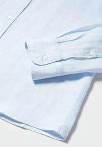 Camisa de lino azul claro con puños abotonados, que presenta una textura suave y un sutil patrón de tejido, diseñada para un ajuste relajado.