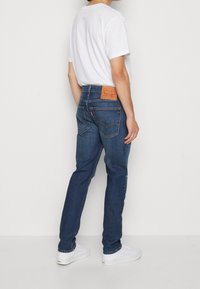 Blå denimjeans med rak passform, med en läderlapp på bakre midjan och två bakfickor, kombinerat med en vit T-shirt och skor.