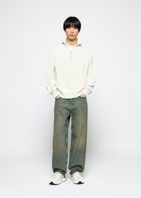 White textured knit sweater with a half-zip collar, paired with loose-fit blue jeans and white sneakers with black accents.