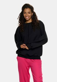 Czarny długi rękaw bluz z okrągłym dekoltem i obszerna rękawami, zestawiony z jasnoróżowymi spodniami. Gładki materiał o luźnym kroju.