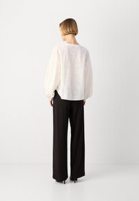 Blusa bianca ricamata con maniche a palloncino e scollo rotondo, abbinata a pantaloni neri a gamba larga, vista da dietro.