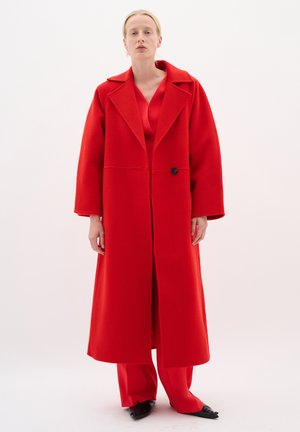 Rode wollen lange jas met brede revers, enkele knoopsluiting en oversized mouwen. Gekocht over een bijpassende rode satijnen outfit en flats.